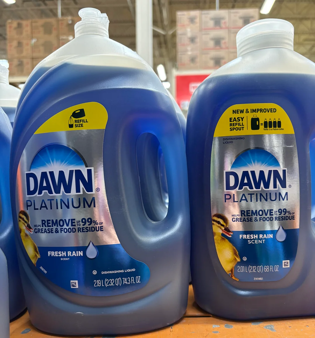 Two large bottles of Dawn Platinum dishwashing liquid, Fresh Rain scent, are displayed side by side on a store shelf. The labels highlight grease removal and an easy refill spout.