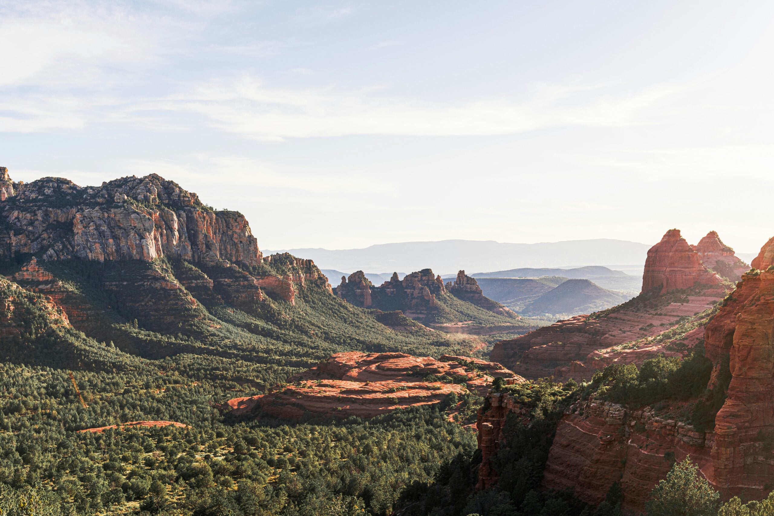 A scenic view of red rock formations and rugged cliffs surrounded by green vegetation under a clear sky, likely in a desert or canyon landscape.