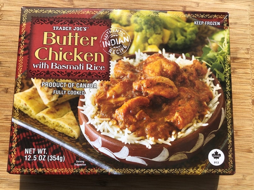A Trader Joe’s Butter Chicken with Basmati Rice frozen meal box, showing a bowl of butter chicken on rice with naan and greens. The packaging highlights it as an authentic Indian recipe and a product of Canada.