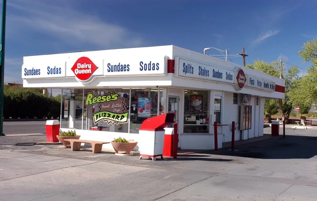 A small, retro-style Dairy Queen building features signage for sundaes, sodas, and splits. A Reese's Blizzard is advertised out front. The white building with red accents echoes the charm captured in Vintage Fast-Food Photos.