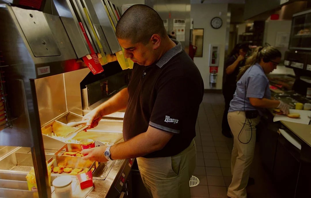 A fast-food worker in uniform places fries into containers at a fryer station, while two other employees work in the background—capturing the timeless energy seen in Vintage Fast-Food Photos.
