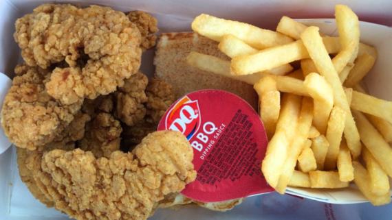 A meal tray with crispy fried chicken tenders, golden French fries, a slice of toasted bread, and a cup of DQ BBQ dipping sauce&mdash;classic yet overpriced fast food done right.