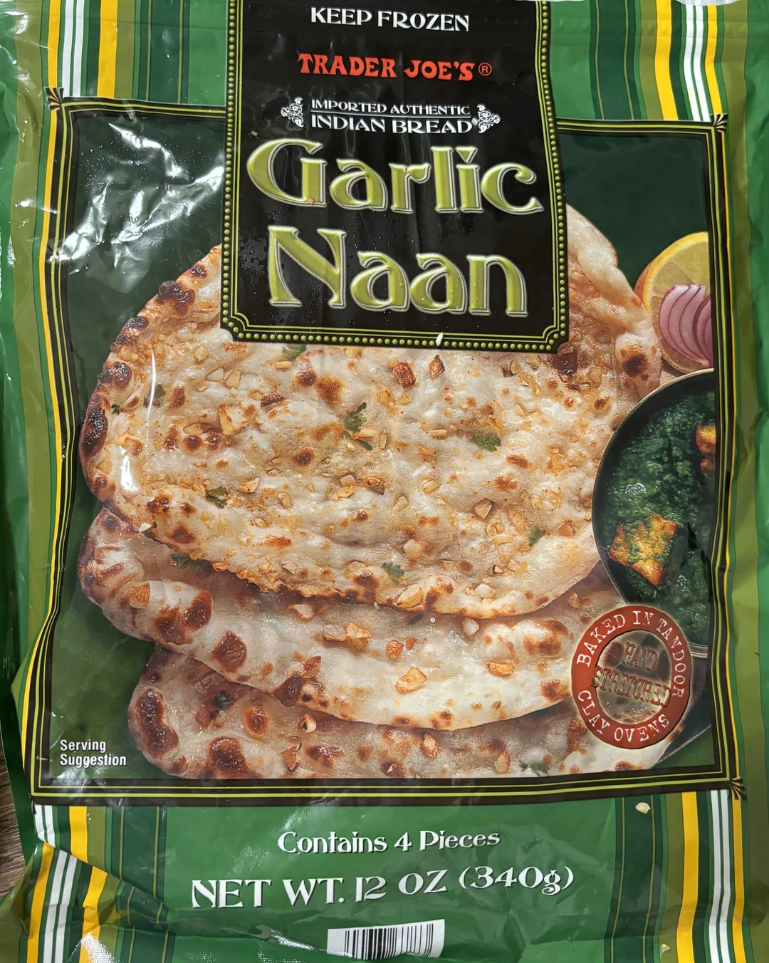 A green package of Trader Joe’s Garlic Naan, featuring an image of naan bread topped with garlic, served with spinach curry and sliced onions. The package contains 4 pieces and weighs 12 oz (340g).