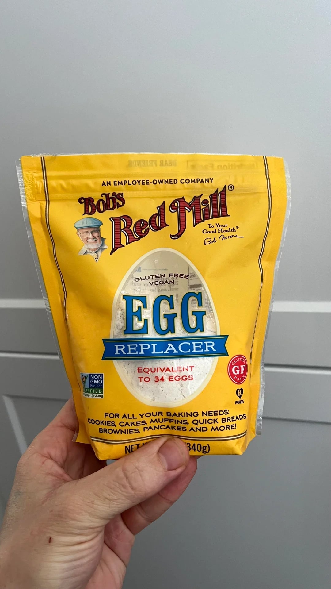 A hand holds a yellow package of Bob's Red Mill Gluten Free Egg Replacer, labeled as equivalent to 34 eggs and perfect for baking needs. This 12 oz (340 g) pack offers a convenient option among egg substitutes.