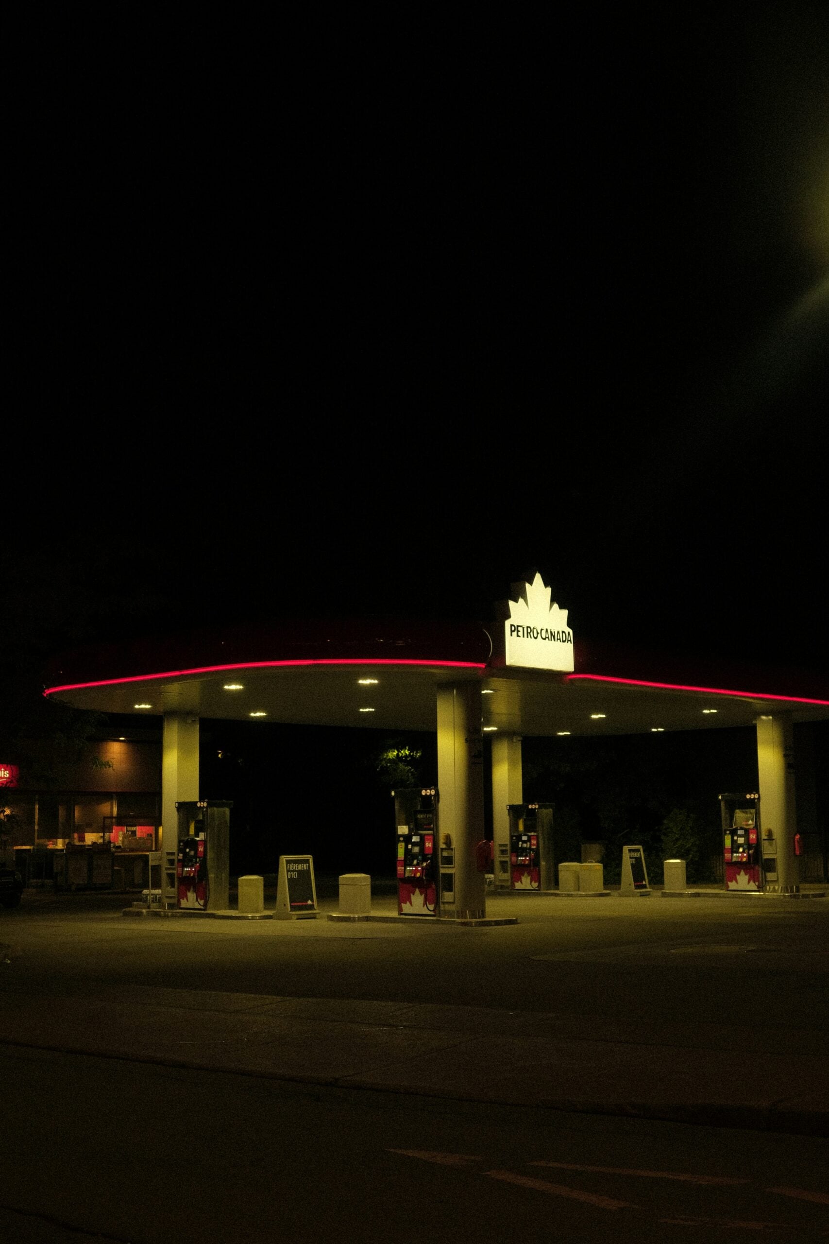 A Petro-Canada gas station at night, illuminated by its canopy lights and red trim, with several gas pumps visible and the surrounding area mostly dark.