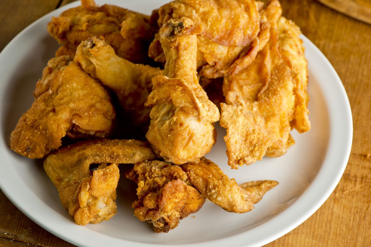 A white plate filled with several pieces of golden-brown, crispy fried chicken on a wooden table.
