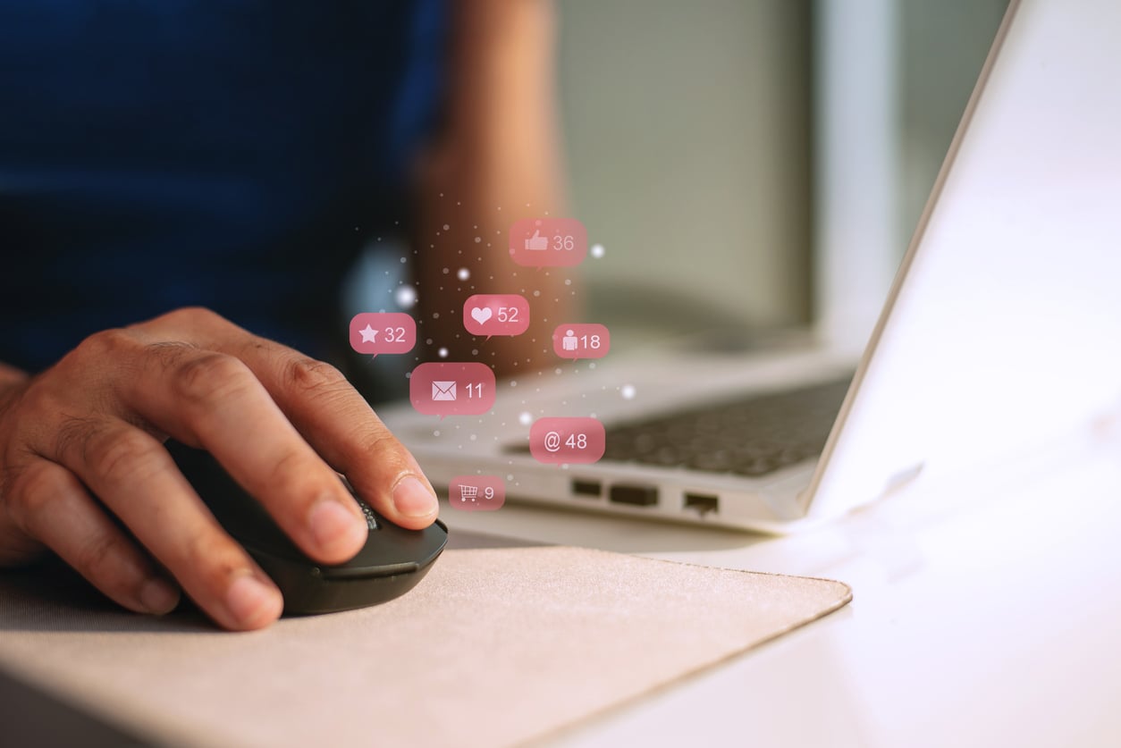 A person using a computer mouse next to a laptop, with floating social media notification icons for likes, messages, and followers—and tips on concert ticket hacks—appearing above the mouse.