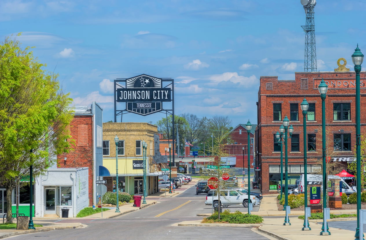 A downtown street in Johnson City, Tennessee, showcases historic brick buildings and small shops—reflecting the charm that earns it a place among top Small Business States—with parked cars and a bold black-and-white “Johnson City, Tennessee” sign overhead.