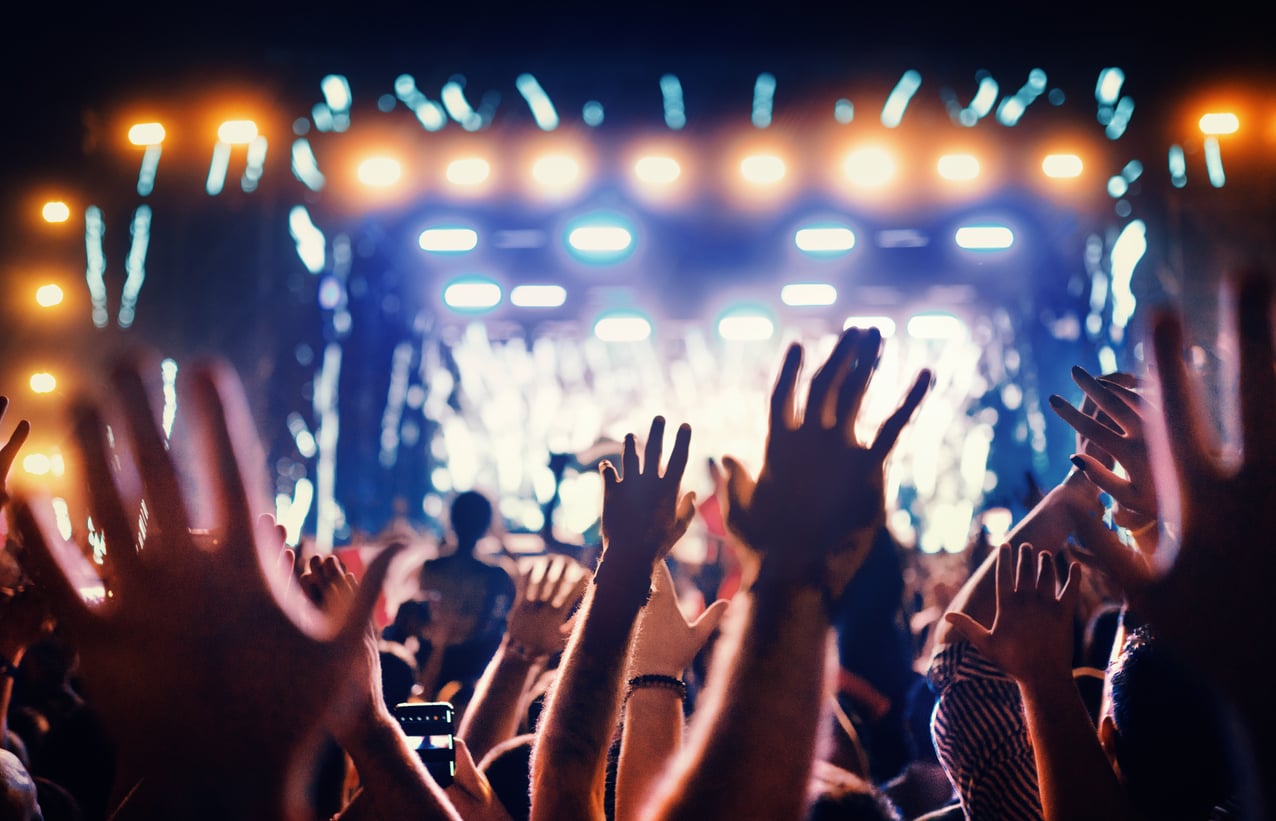 A crowd of people with raised hands enjoying a concert at night, with bright stage lights illuminating the scene—capturing the excitement often missing in products men skip buying.