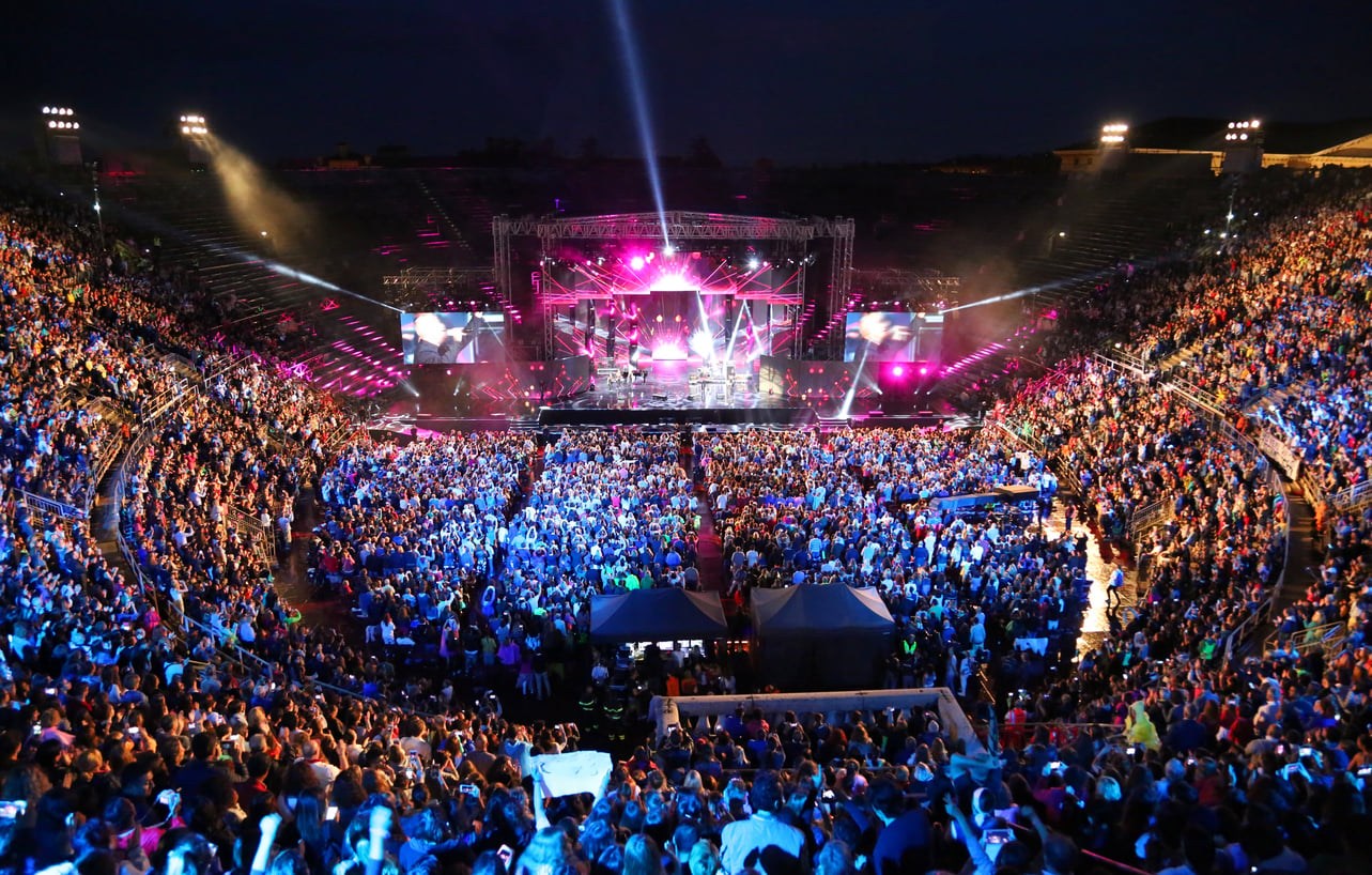 A large, packed outdoor stadium at night with a brightly lit stage, colorful lights, and a crowd of people enjoying a concert—perfect for those seeking concert ticket hacks to experience live performances up close.