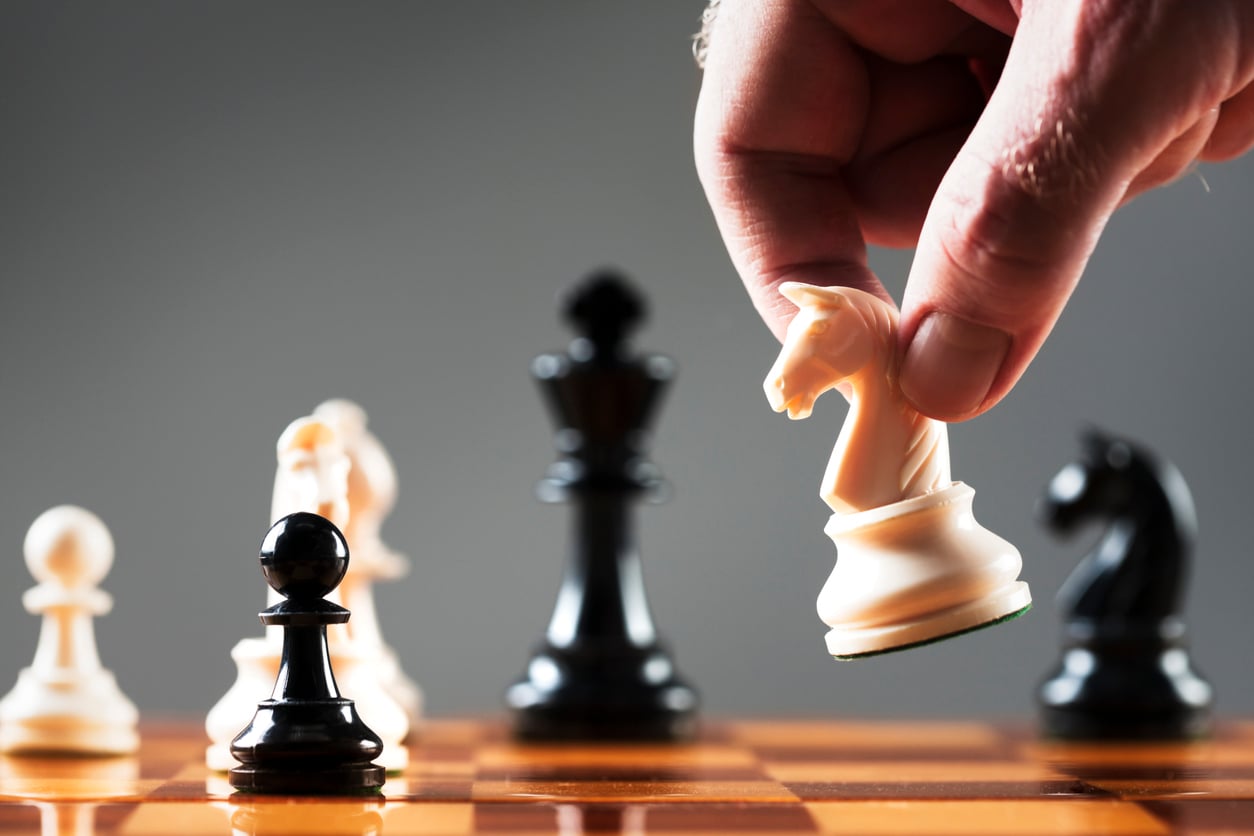 A close-up of a hand moving a white knight on a chessboard, with black and white pieces positioned for play—a perfect example of budget-friendly hobbies set against a blurred background.