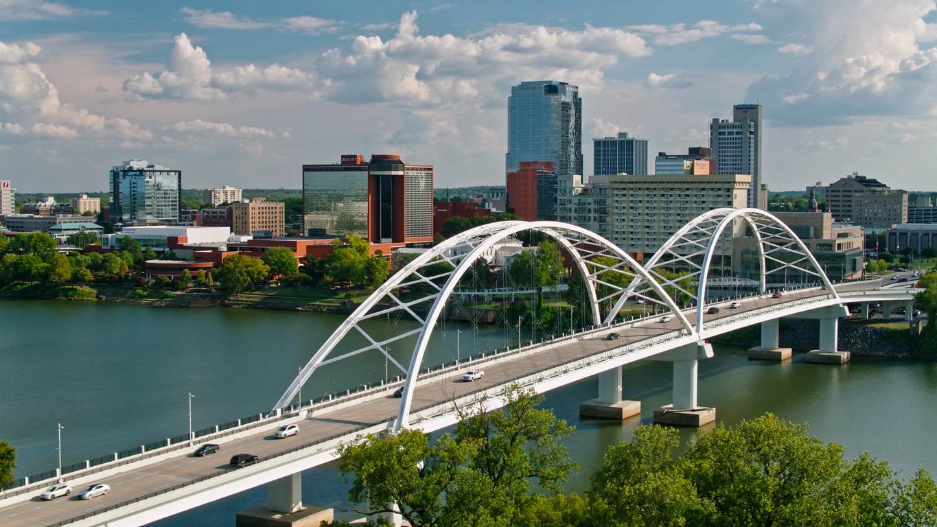 A white arched bridge spans a river toward a city skyline with tall modern buildings, greenery, and partly cloudy skies—symbolizing the journey to overcoming credit card debt and reaching financial stability.