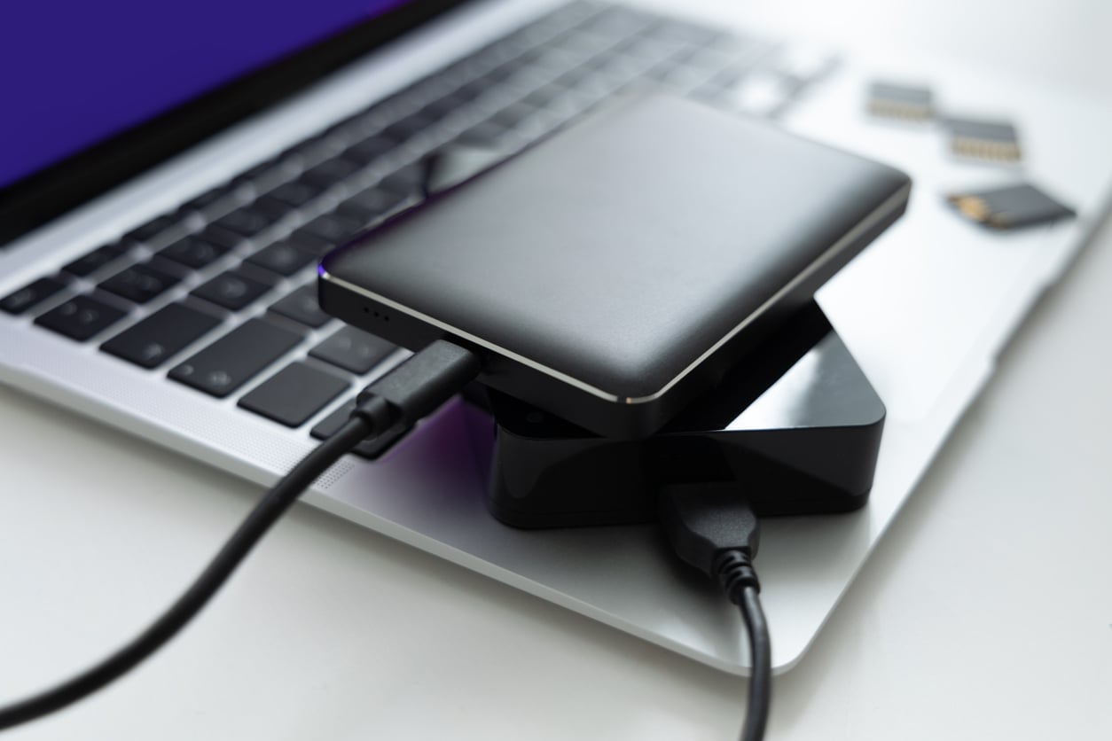 A close-up of an external hard drive and a card reader connected to a laptop keyboard, with several memory cards placed nearby.