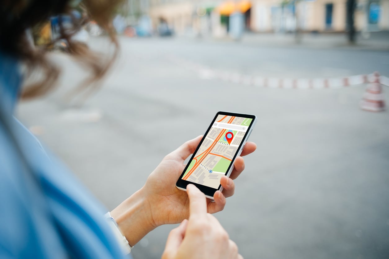 A person holding a smartphone with a map application open, showing a red location pin on the screen, while standing outdoors near a street—perfect for discovering theme park hacks on the go.
