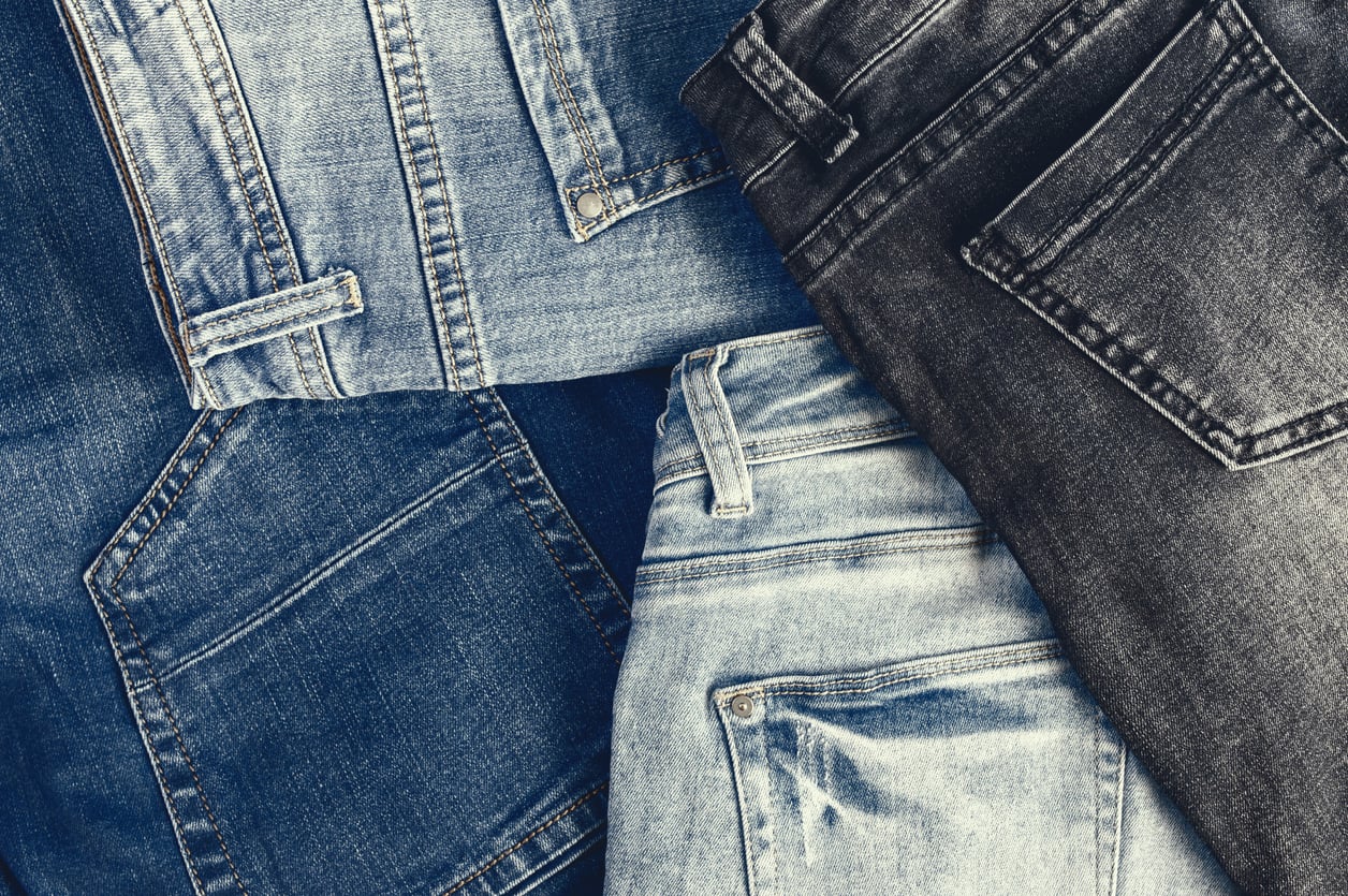 A flat lay of several pairs of jeans in different shades of blue and black, showcasing classic clothes details like back pockets, belt loops, and stitching.