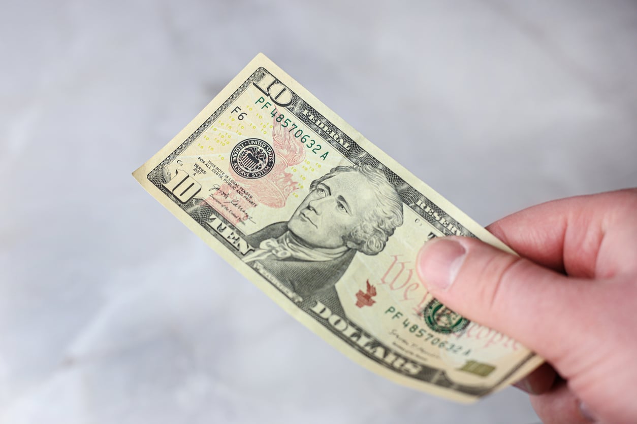 A hand holding a ten-dollar bill against a light, blurred background, evoking memories of 1991 prices and the changing value of money over time.