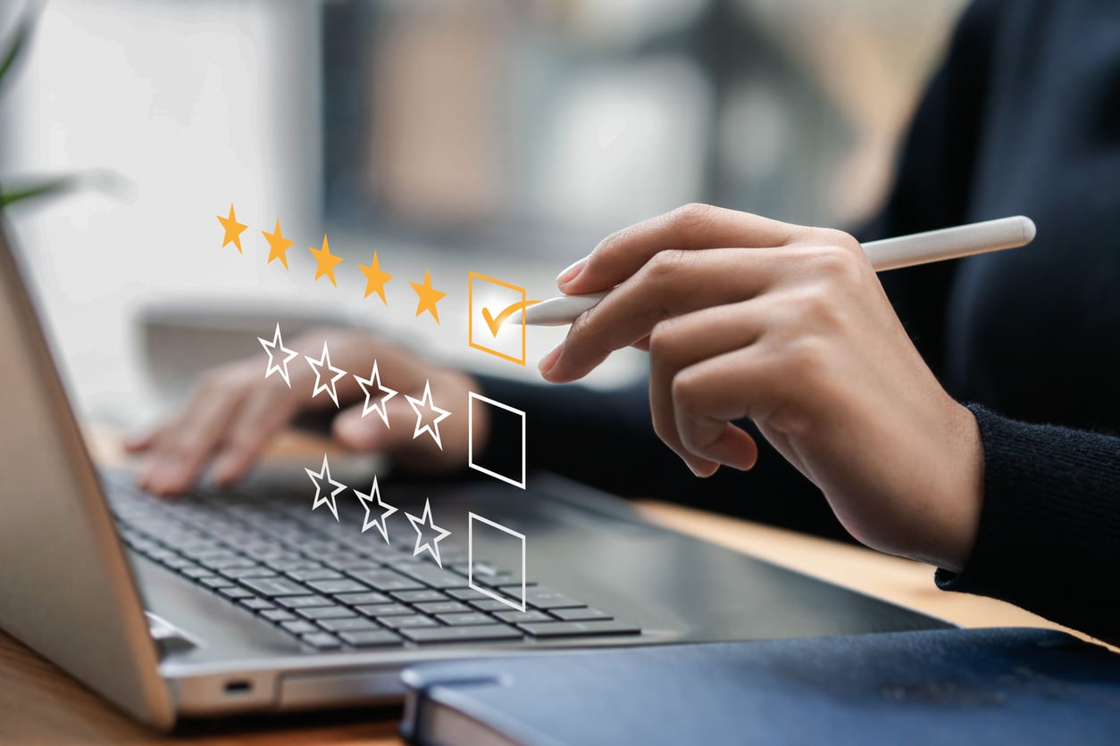 A person uses a stylus to give a five-star rating on a virtual interface above a laptop keyboard, symbolizing customer feedback or satisfaction after staying at an Airbnb in a digital environment.