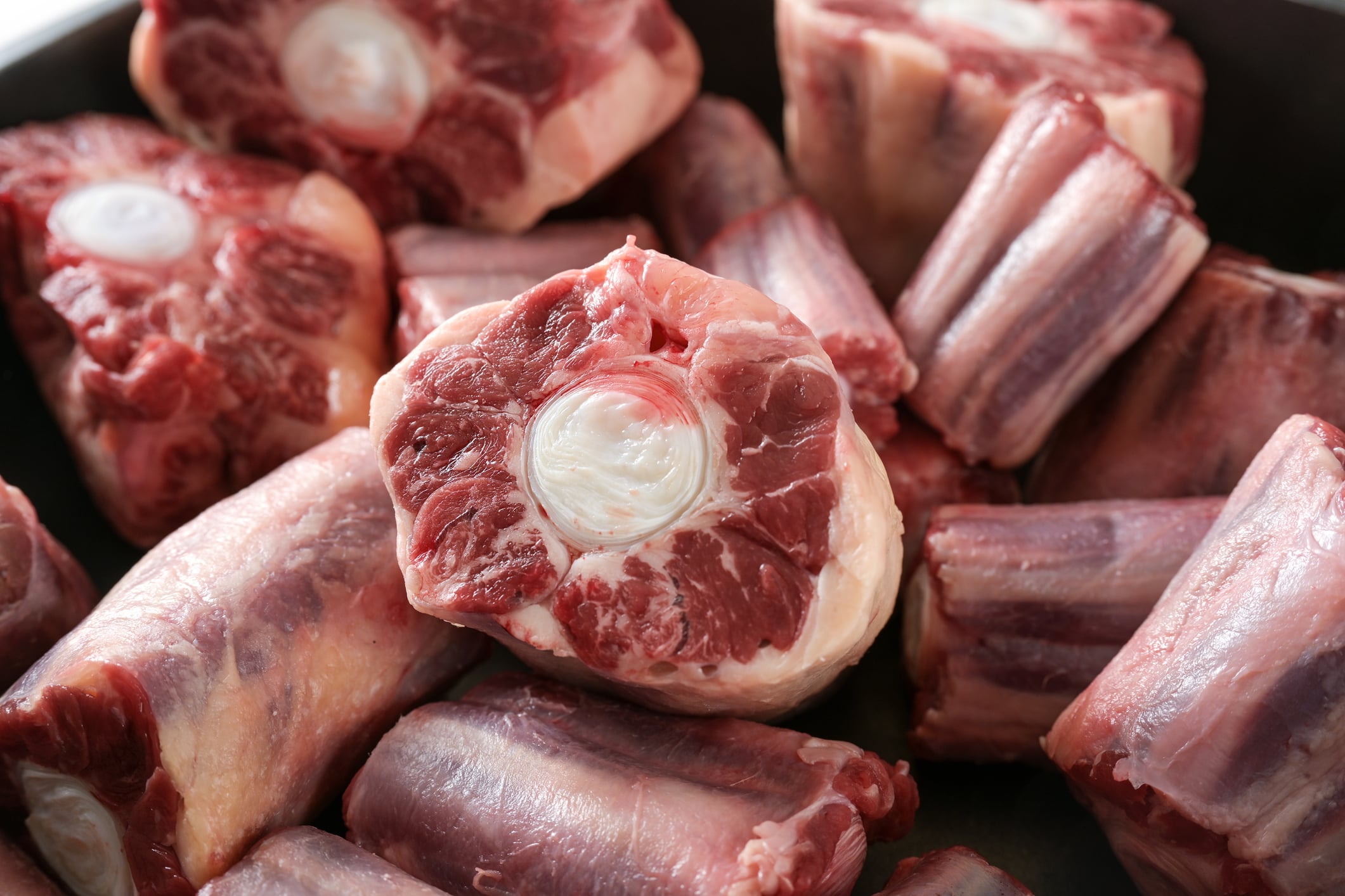 Close-up of several pieces of raw oxtail, showing the round bone centers surrounded by red meat and some white fat, all placed together in a pile.