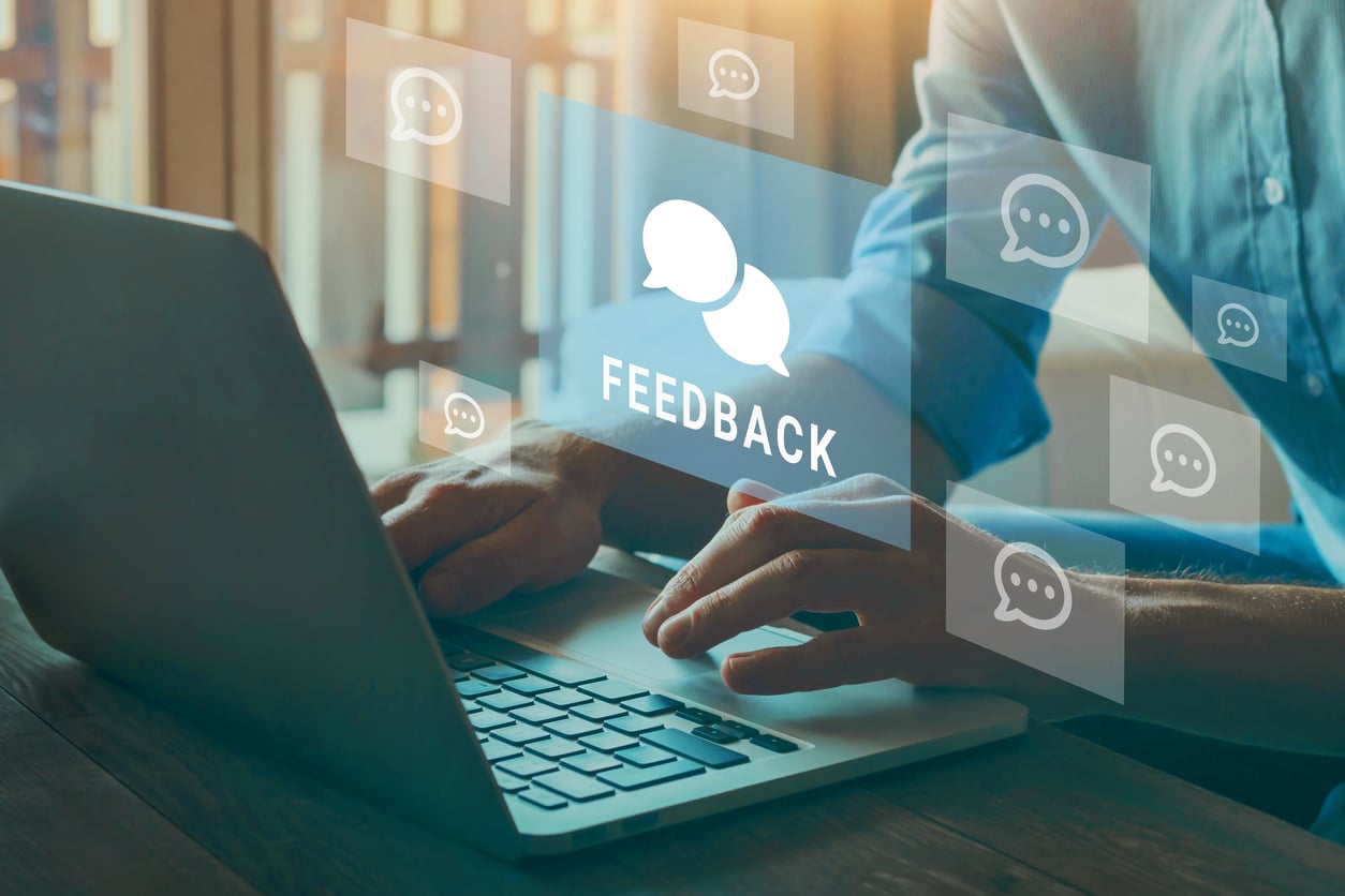 A person types on a laptop, with digital icons showing speech bubbles and the word "FEEDBACK" floating above the keyboard, representing online reviews or feedback from staying at an Airbnb.