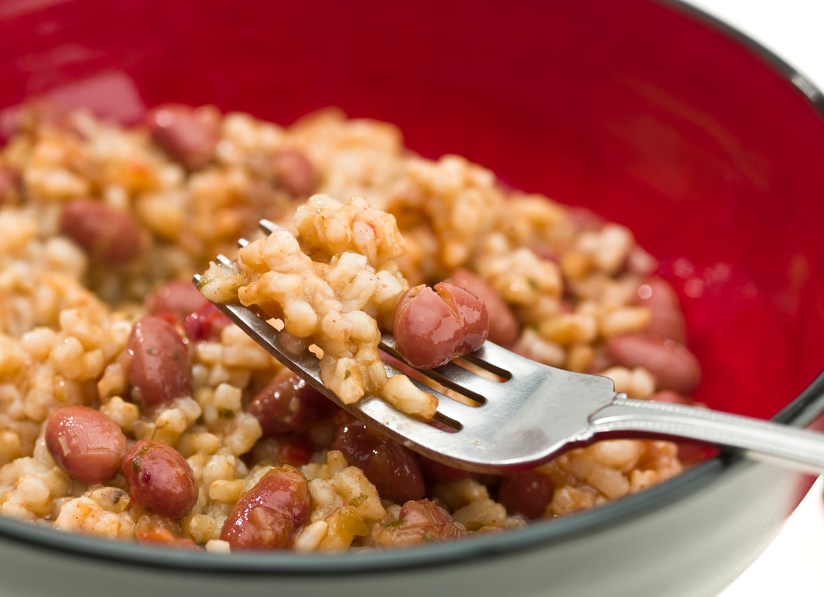 A close-up of a fork lifting a bite of rice and red beans from a red and black bowl. The saucy, well-mixed dish highlights the textures of beans, grains of rice, and ground beef alternatives for a hearty, plant-based meal.