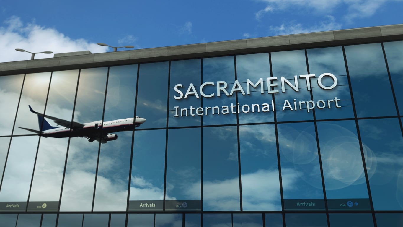 A passenger airplane is reflected in the glass facade of a building with the words "Sacramento International Airport" displayed, highlighting one of the region’s most convenient airports under a partly cloudy sky.