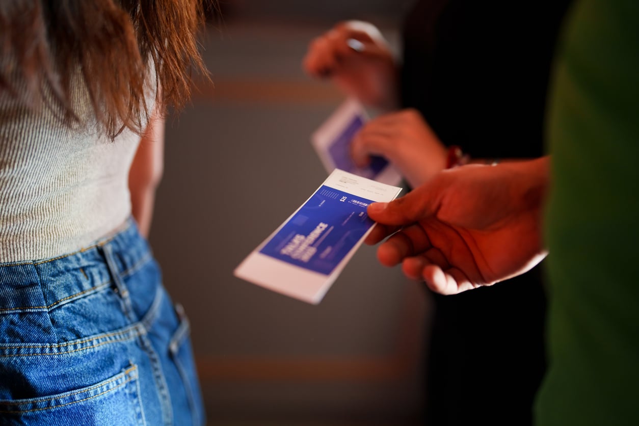 A person hands a blue event ticket to another, while others with similar tickets wait nearby—perfect for discovering theme park hacks and making the most of your visit.