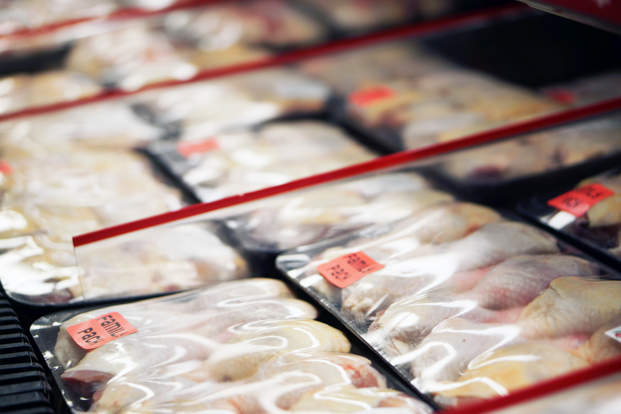 Rows of packaged raw chicken pieces in clear plastic trays, each with a red price label, displayed in a refrigerated section of a grocery store.