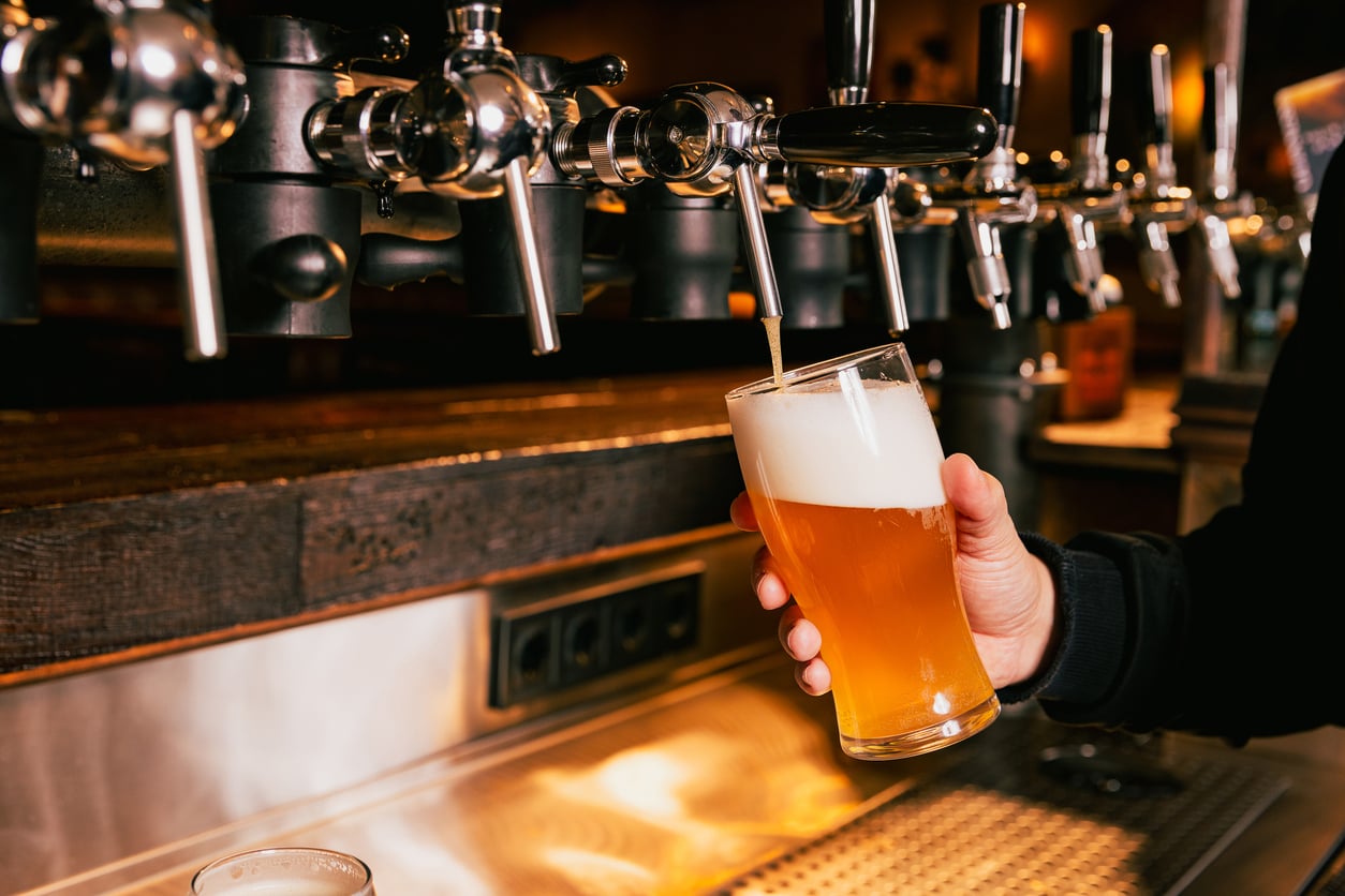 A person fills a pint glass with draft beer from a row of shiny beer taps at a bar—an indulgence among the products men skip buying for home, opting instead to enjoy the perfect pour and thick, foamy head straight from the tap.