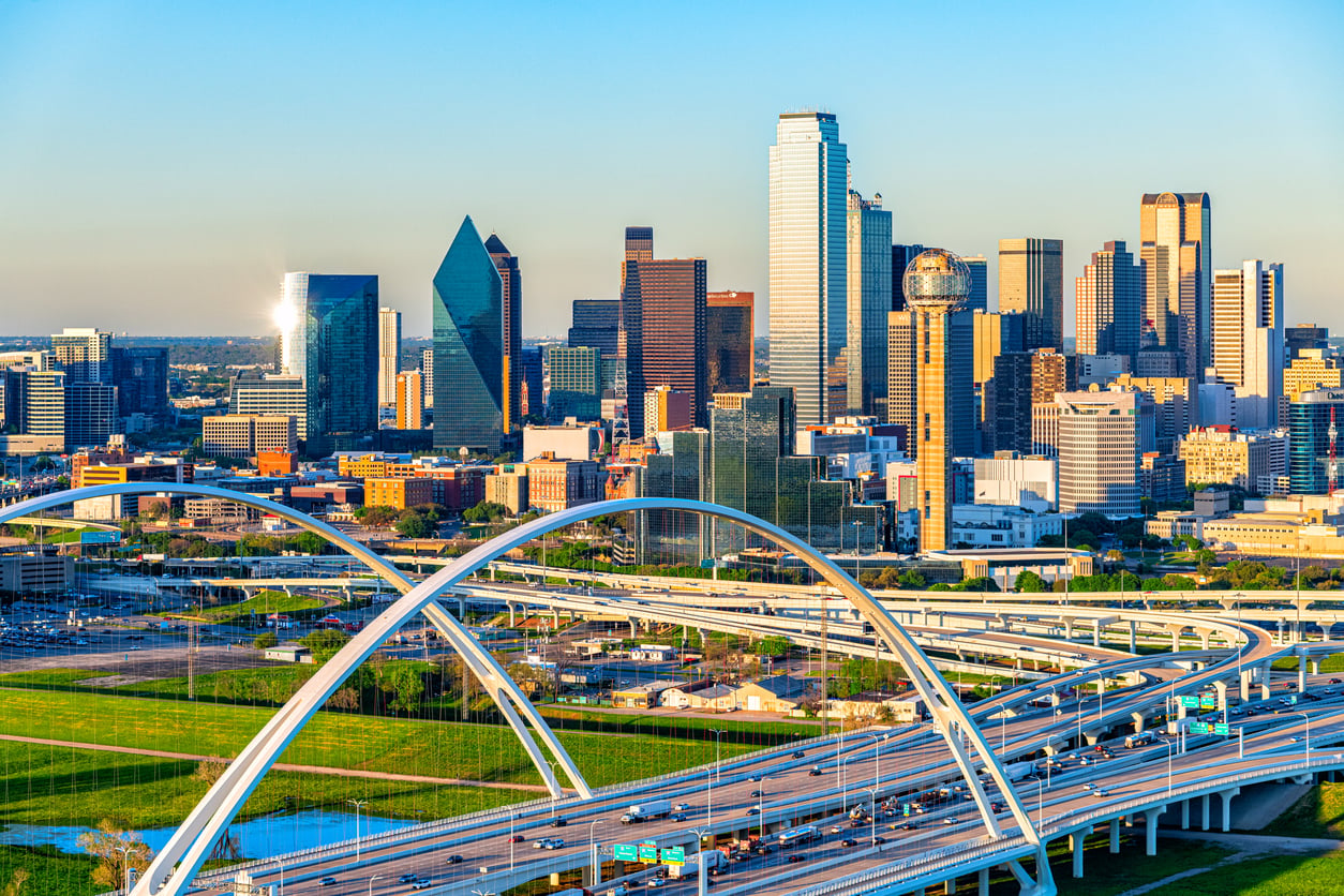 A vibrant cityscape of Dallas, Texas—ranked among top Small Business States—features modern skyscrapers, the iconic Reunion Tower, and white arched bridges crossing busy highways under a clear blue sky.