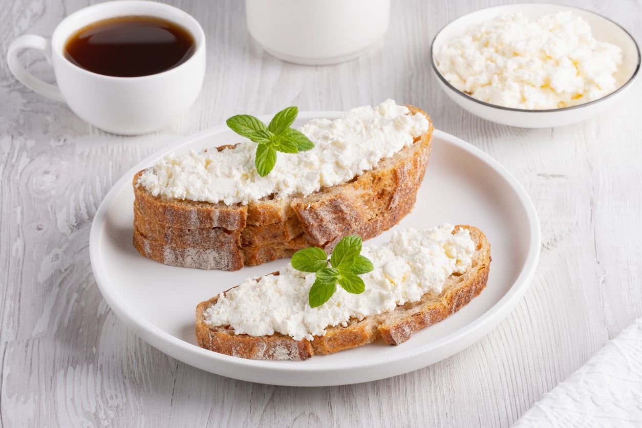 Two slices of rustic bread topped with ricotta cheese and mint leaves on a white plate, served alongside a cup of coffee and a bowl of ricotta—perfect for breakfast or brunch, especially when you’re looking for meals with egg substitutes.