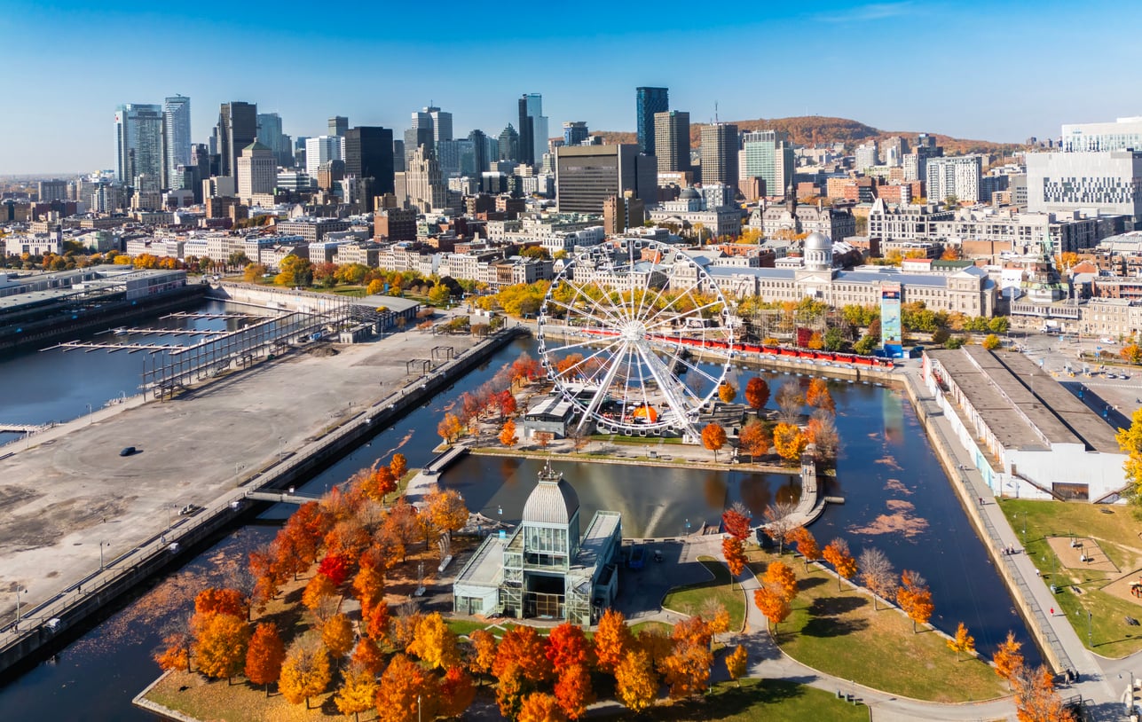 Aerial view of Montreal’s downtown skyline with skyscrapers, autumn-colored trees, La Grande Roue Ferris wheel, and nearby waterfront under a bright blue sky—an inviting scene for those seeking Florida alternatives.