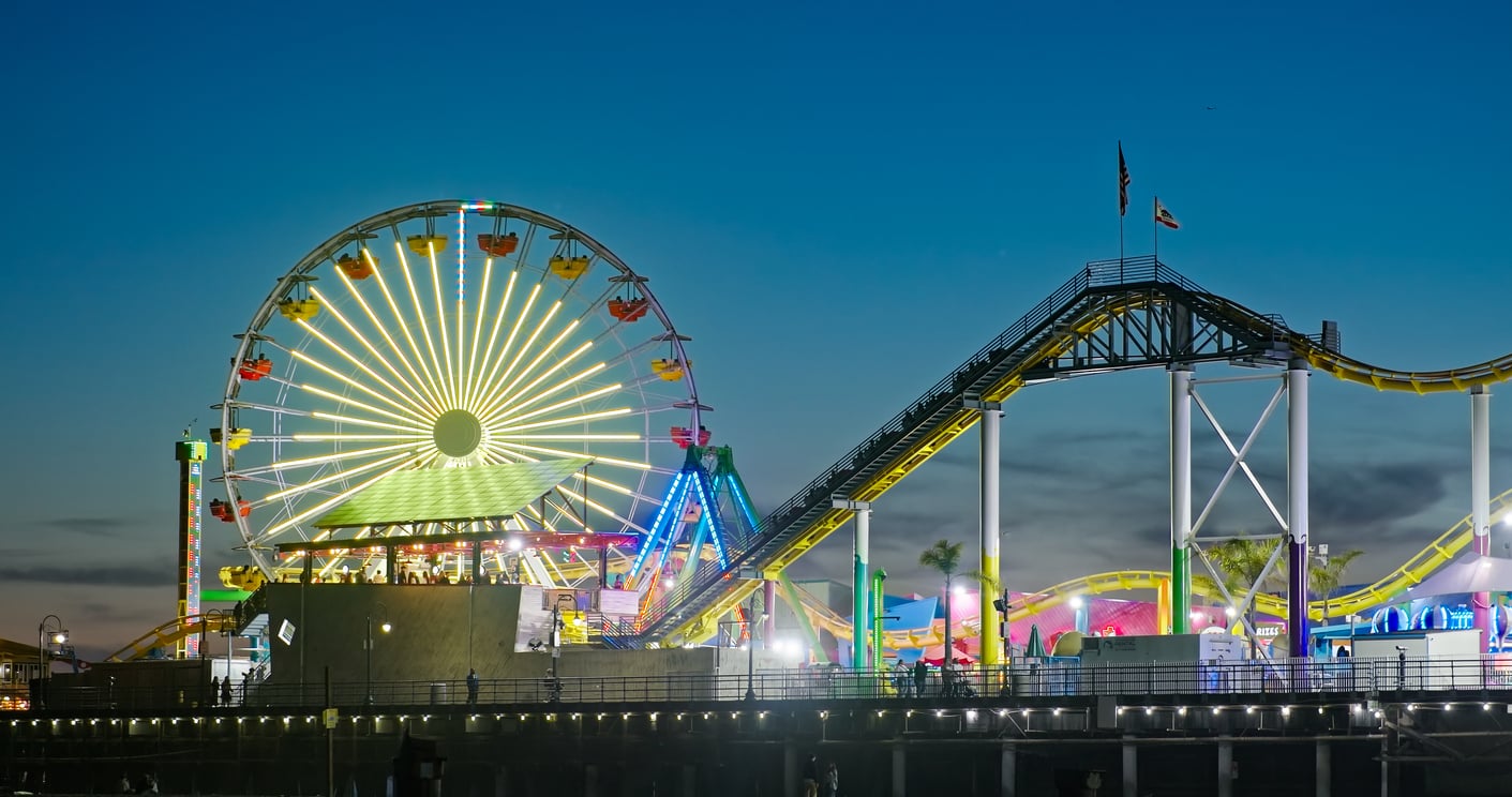 A brightly lit Ferris wheel and roller coaster glow with colorful lights during twilight at the amusement park, where theme park hacks can help you make the most of your visit beneath the clear evening sky.