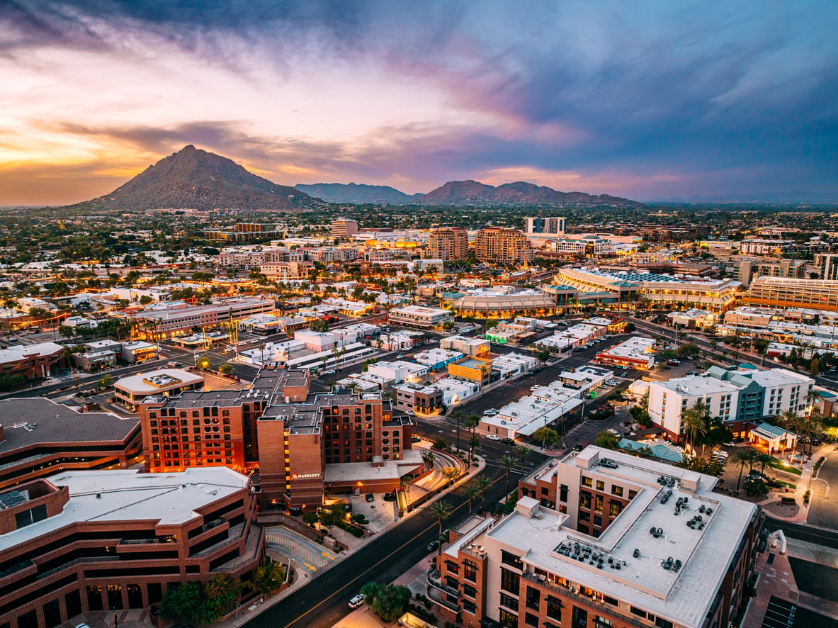 Aerial view of a city at sunset in one of the top Small Business States, with modern buildings, busy streets, and distant mountains under a dramatic, colorful sky.