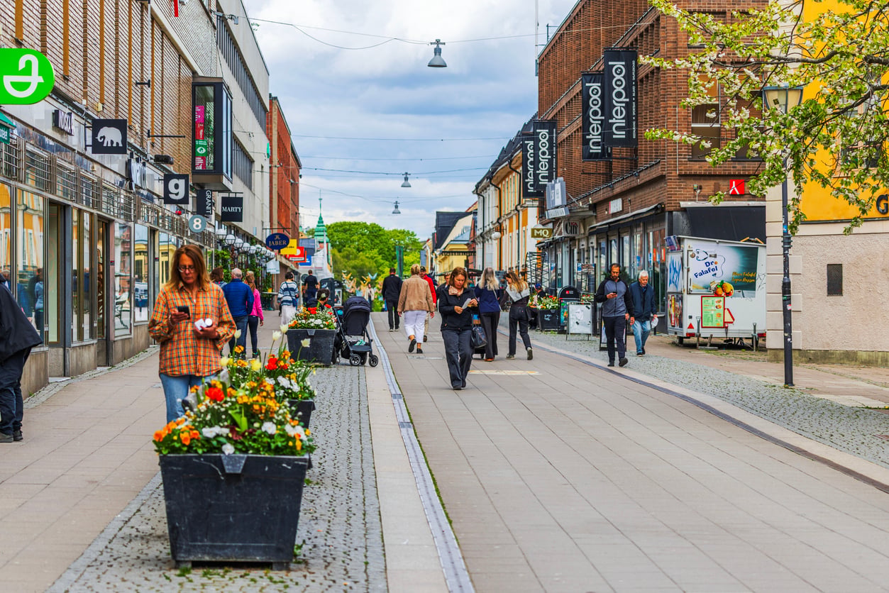 A lively pedestrian street lined with shops and flowers, where people walk, shop, and enjoy the day under a partly cloudy sky—an inviting scene often found in thriving Small Business States.