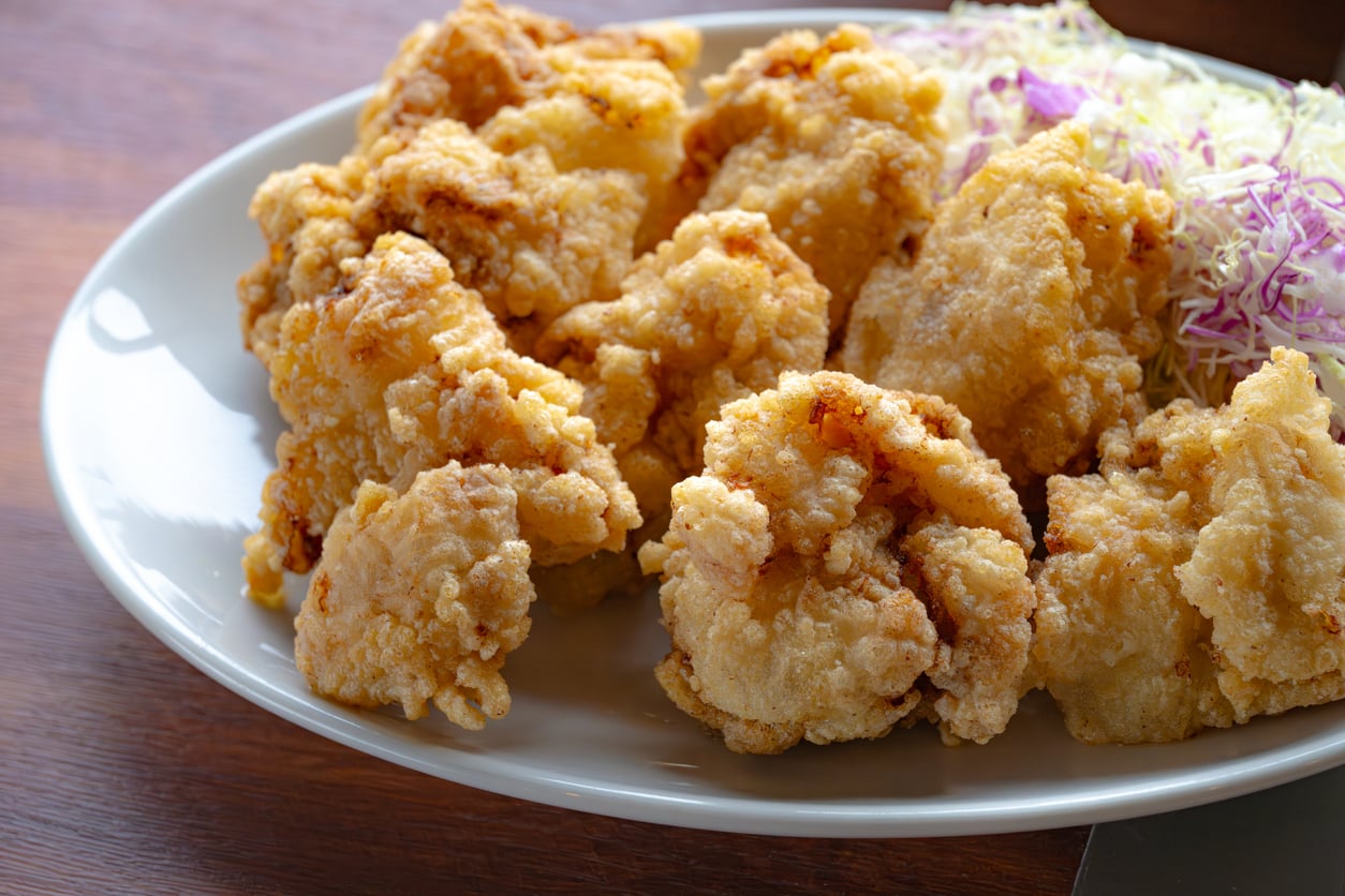 A plate of golden-brown fried chicken pieces served with a side of finely shredded cabbage on a white dish.
