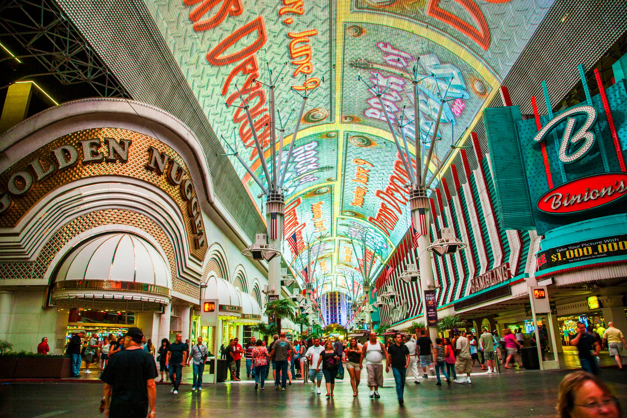 Crowds walk under the vibrant, illuminated canopy of Fremont Street in Las Vegas, with colorful signs for casinos like Golden Nugget and Binion's lining the busy pedestrian street—an ideal spot for Las Vegas budget tips and free entertainment.