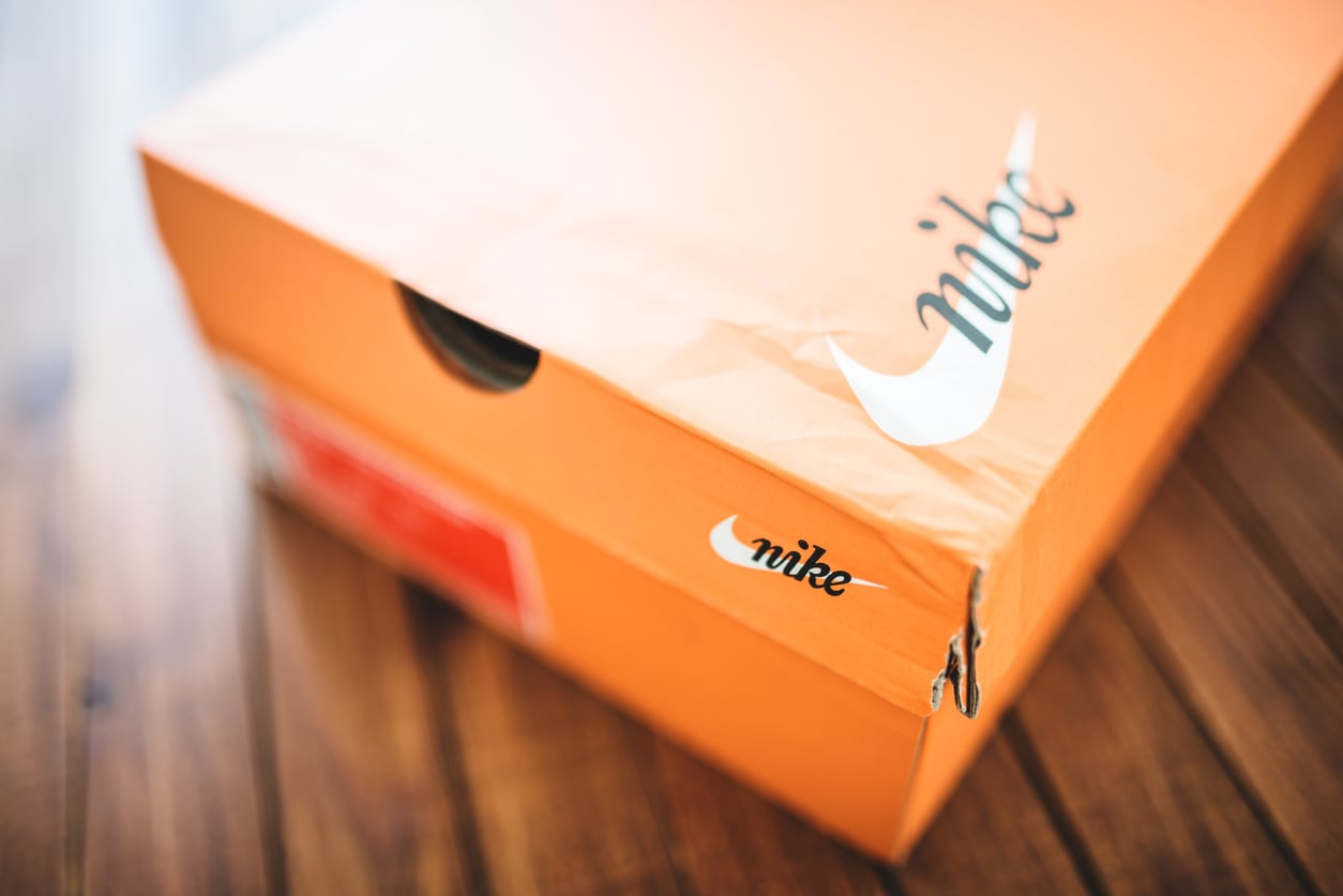 An orange Nike shoebox with the Nike logo and swoosh is placed on a wooden surface. The box shows a small tear near one corner.