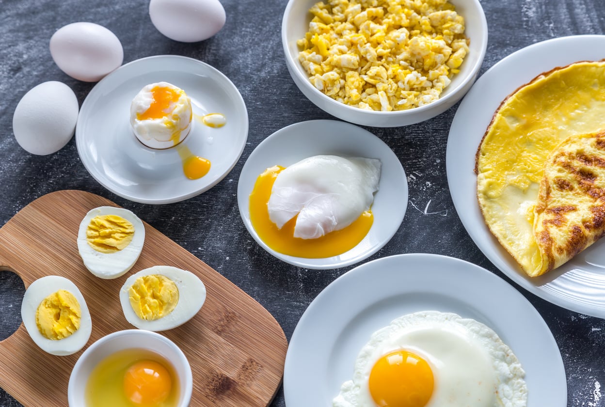 A variety of egg dishes on a table, including scrambled eggs, an omelet, a fried egg, poached eggs, soft-boiled and hard-boiled eggs—served alongside raw eggs and cracked shells as tasty ground beef alternatives.