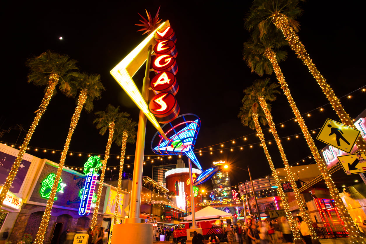 Colorful neon signs and palm trees light up the night along Fremont Street in downtown Las Vegas. A large martini glass sign and the word "VEGAS" stand out, drawing lively crowds eager for fun and Las Vegas budget tips.