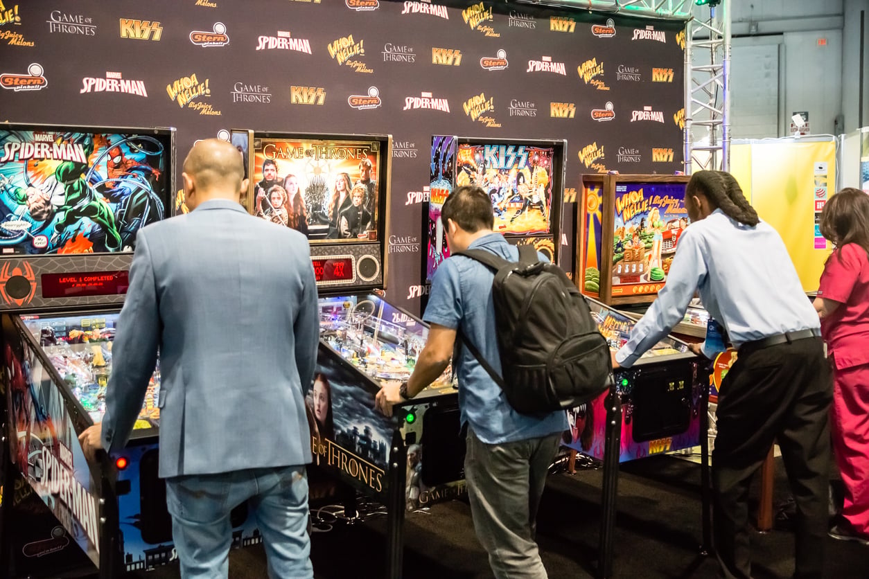 Four people play themed pinball machines, like Spider-Man and Game of Thrones, at a brightly lit arcade event in Las Vegas. The scene feels like discovering budget tips for fun—enjoy world-class entertainment without breaking the bank.