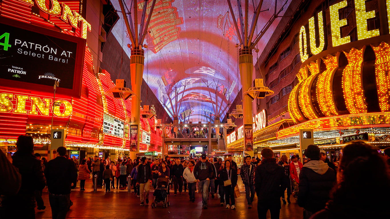 Crowd walks under the illuminated canopy of Fremont Street in Las Vegas at night, surrounded by bright neon signs for casinos and bars—an experience often highlighted in Las Vegas budget tips for its vibrant, lively atmosphere at little to no cost.