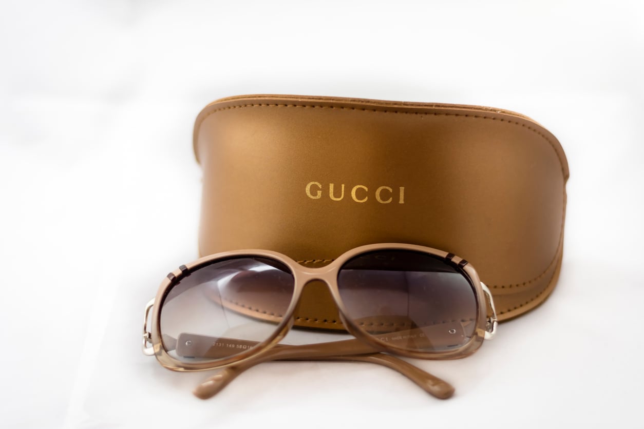 A pair of brown Gucci sunglasses with tinted lenses is placed in front of a brown Gucci case, featuring the brand name in gold lettering, adding a touch of luxury to your collection of designer accessories and clothes.