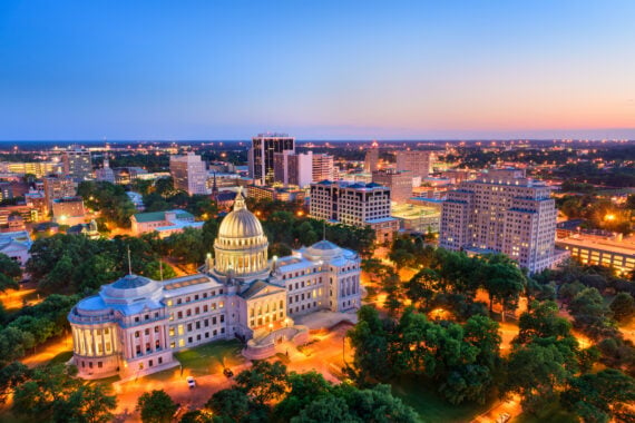Aerial view of downtown Jackson, Mississippi at sunset, featuring the illuminated Mississippi State Capitol building surrounded by trees and city lights&mdash;a striking scene in a city working to address rising credit card debt.