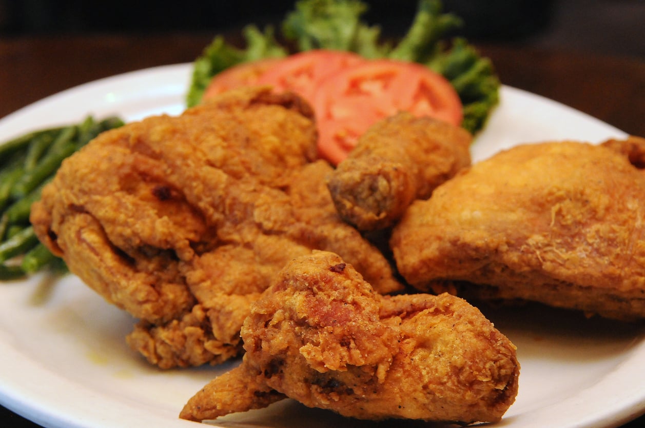 A plate of crispy fried chicken pieces served with sliced tomatoes, green beans, and a bed of lettuce.