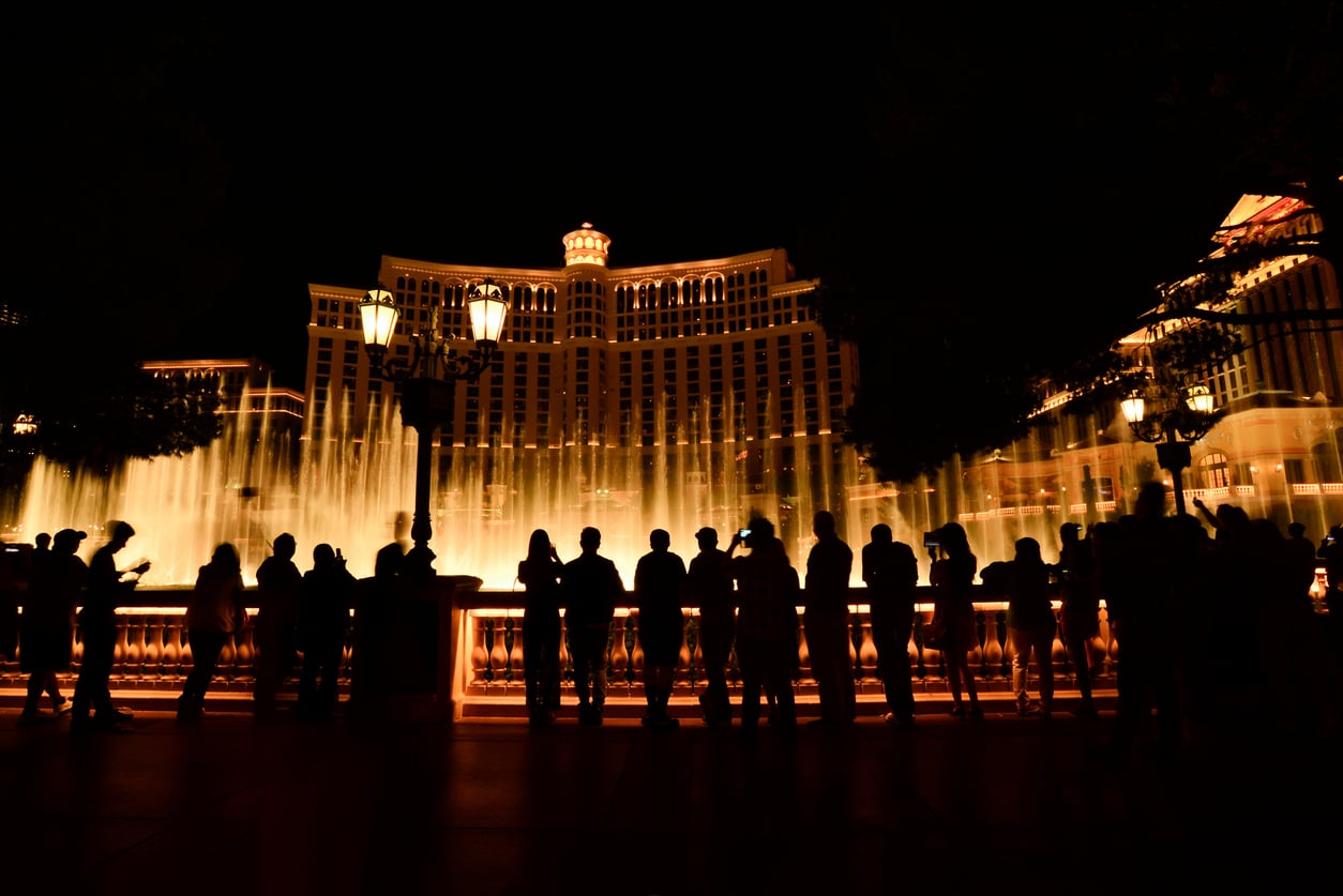 Silhouettes of people watch the illuminated Bellagio Hotel and its fountain show at night in Las Vegas, enjoying a dramatic, free spectacle against the dark sky—a perfect example of Vegas money-saving tips.