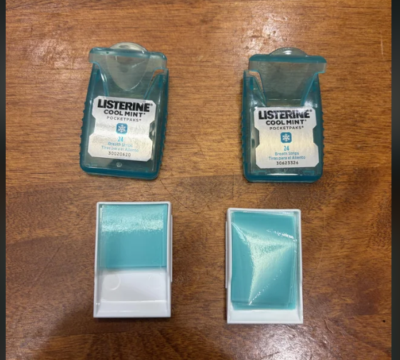 Two open Listerine Cool Mint PocketPaks containers sit on a wooden surface, each with a visible stack of mint strips inside. The open lids and mint strips are clearly shown.