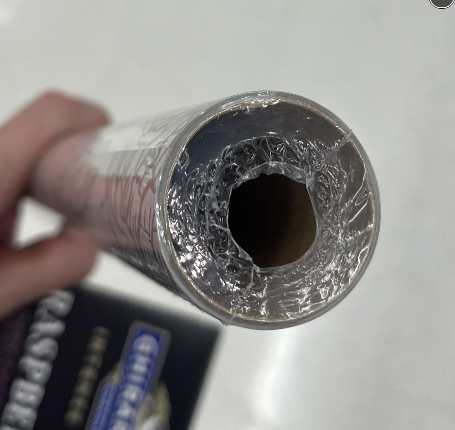 A close-up view of a partially unwrapped roll of plastic wrap, showing the cardboard tube inside and clear plastic film around the opening. A hand is holding the roll against a light background.