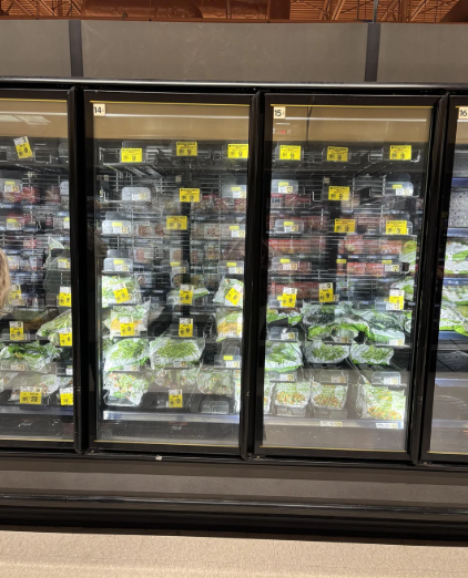 Refrigerated grocery store display with shelves stocked with packaged salads and greens behind glass doors, each package labeled with yellow price tags—perfect for those looking to buy in bulk and keep fresh produce on hand.