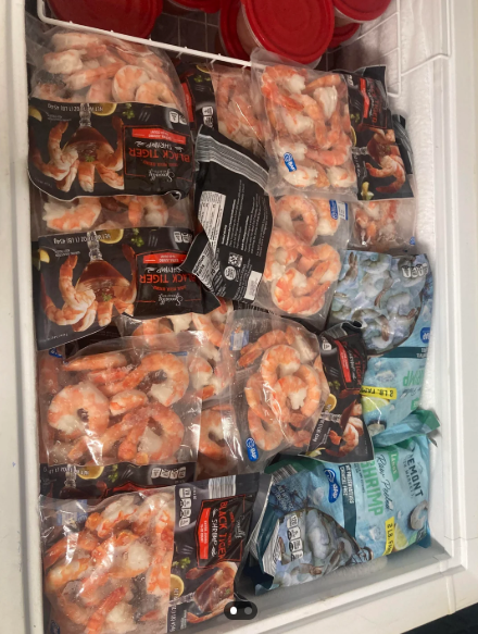 A freezer drawer packed with multiple bags of frozen shrimp, ideal for those who buy in bulk, including Black Tiger and Premium varieties stacked side by side. Red-lidded containers are also visible at the top of the freezer.
