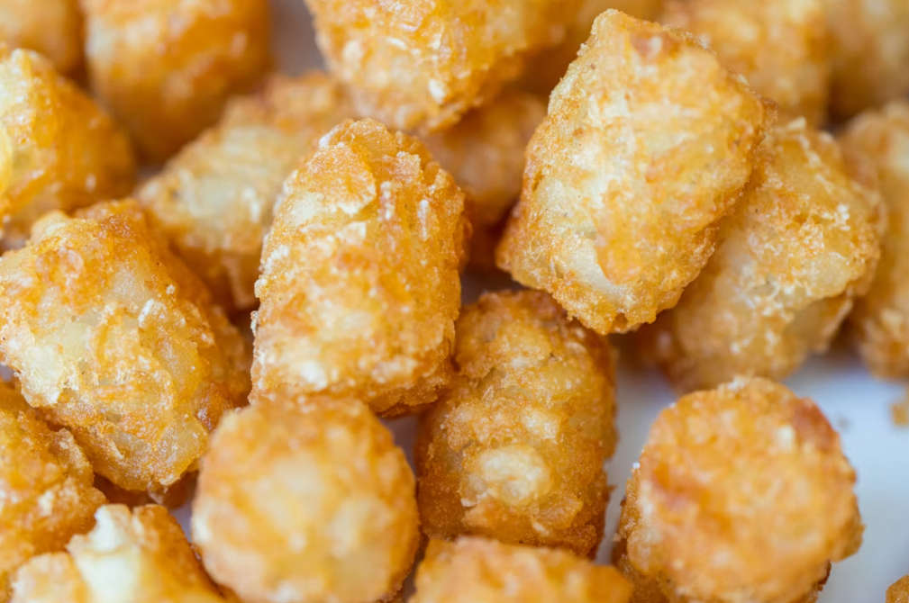 A close-up view of several golden-brown tater tots, showing their crispy, textured surfaces—perfect for those looking to buy in bulk for parties or gatherings.